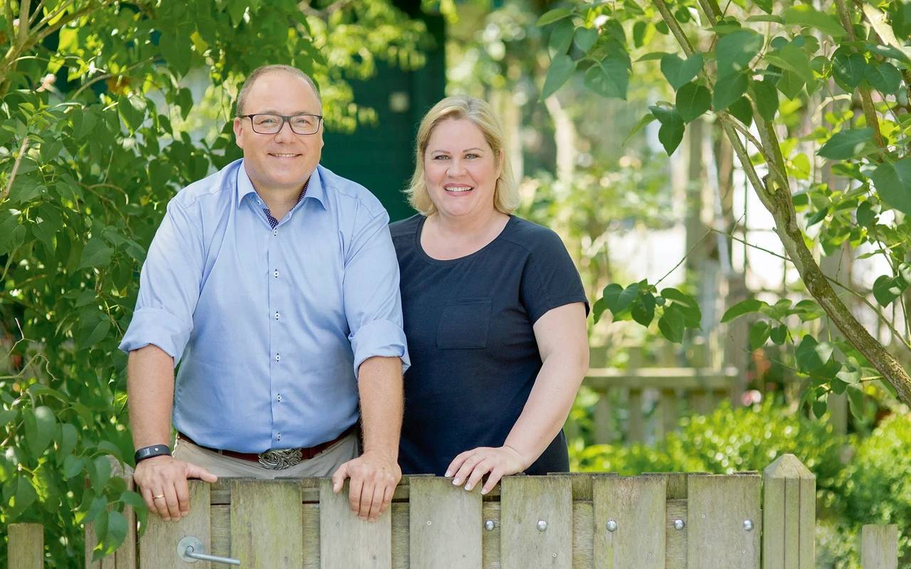 Die Eheleute Dinger stehen im Vordergrund des Bildes. Ein niedriger Zaun reicht Ihnen bis zur Hüfte. Im Hintergrund sind viele Grüne Pflanzen.