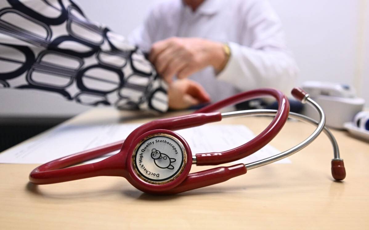 Ein Arzt misst in einer Bereitschaftspraxis in einem Krankenhaus in einem Untersuchungsraum bei einer Patientin den Blutdruck (gestellte Szene). Im Vordergrund liegt ein Stethoskop. (zu dpa: «Bürgermeister laufen Sturm gegen Pläne zu Notfallpraxen»)