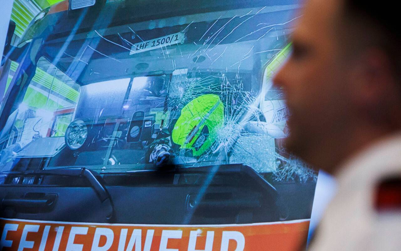 Ein Berliner Feuerwehrmann spricht vor der Darstellung eines beschädigten Feuerwehrwagens von seinen Erlebnissen in einer Silvesternacht.