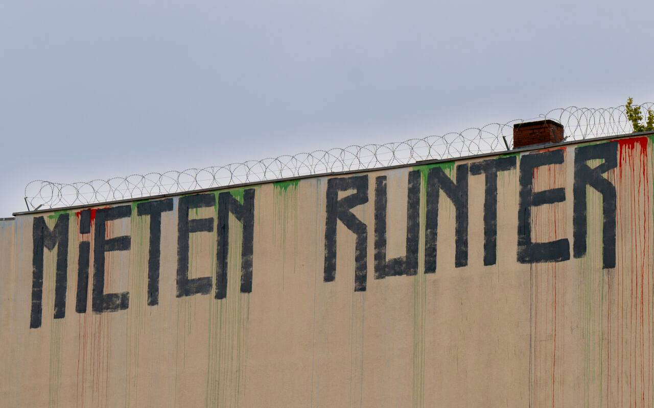 Der Schriftzug "Mieten runter" ist an der Wand eines Miethauses mit Graffiti beschmiert