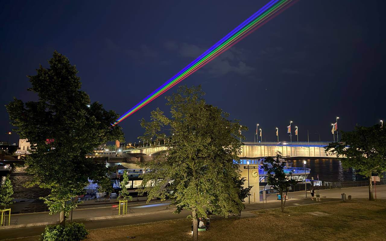 Ein Laser über Deutz und den Rhein in Regenbogenfarben.