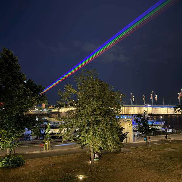 Ein Laser über Deutz und den Rhein in Regenbogenfarben.