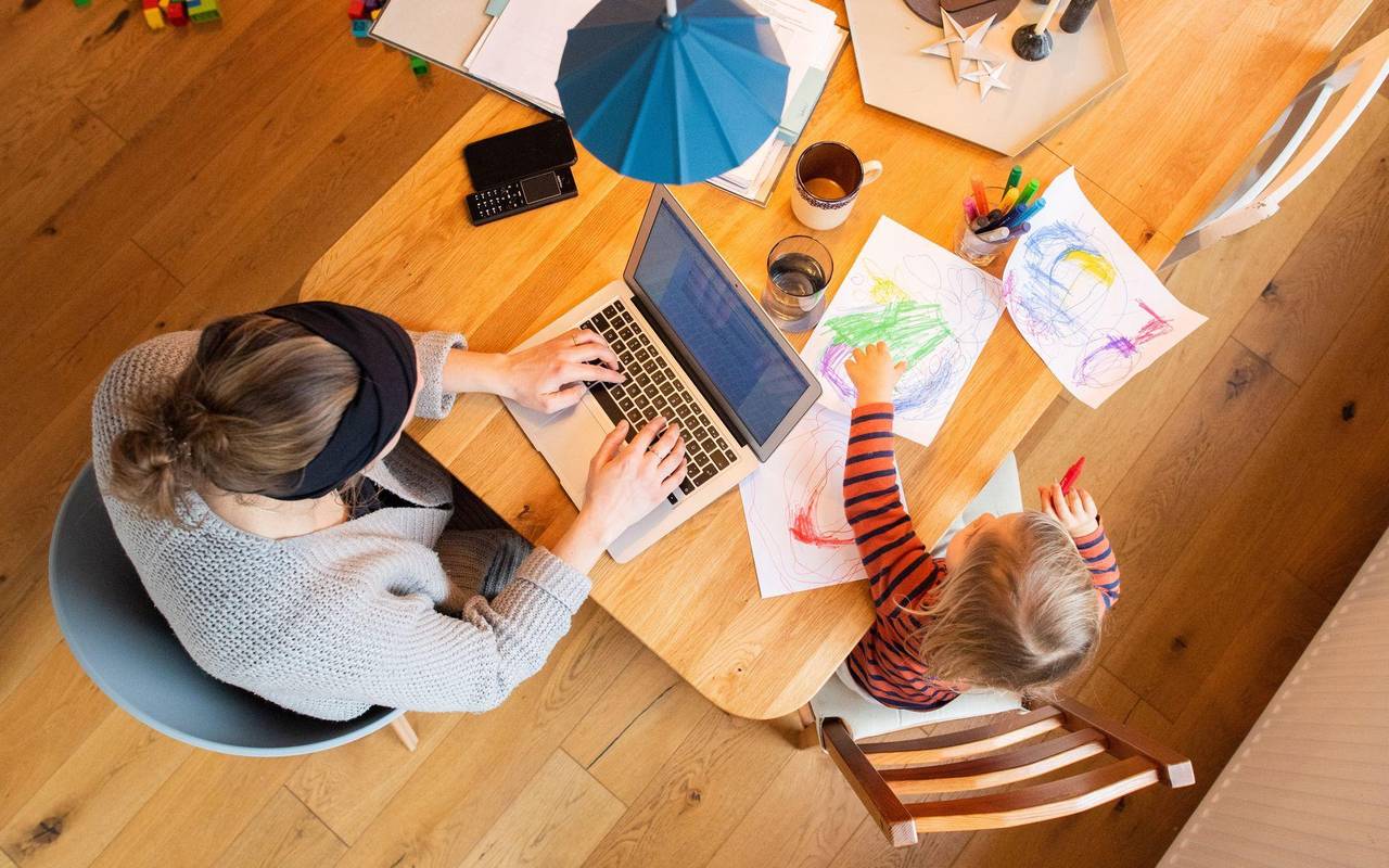Eine Frau arbeitetneben ihrem Kind am Laptop