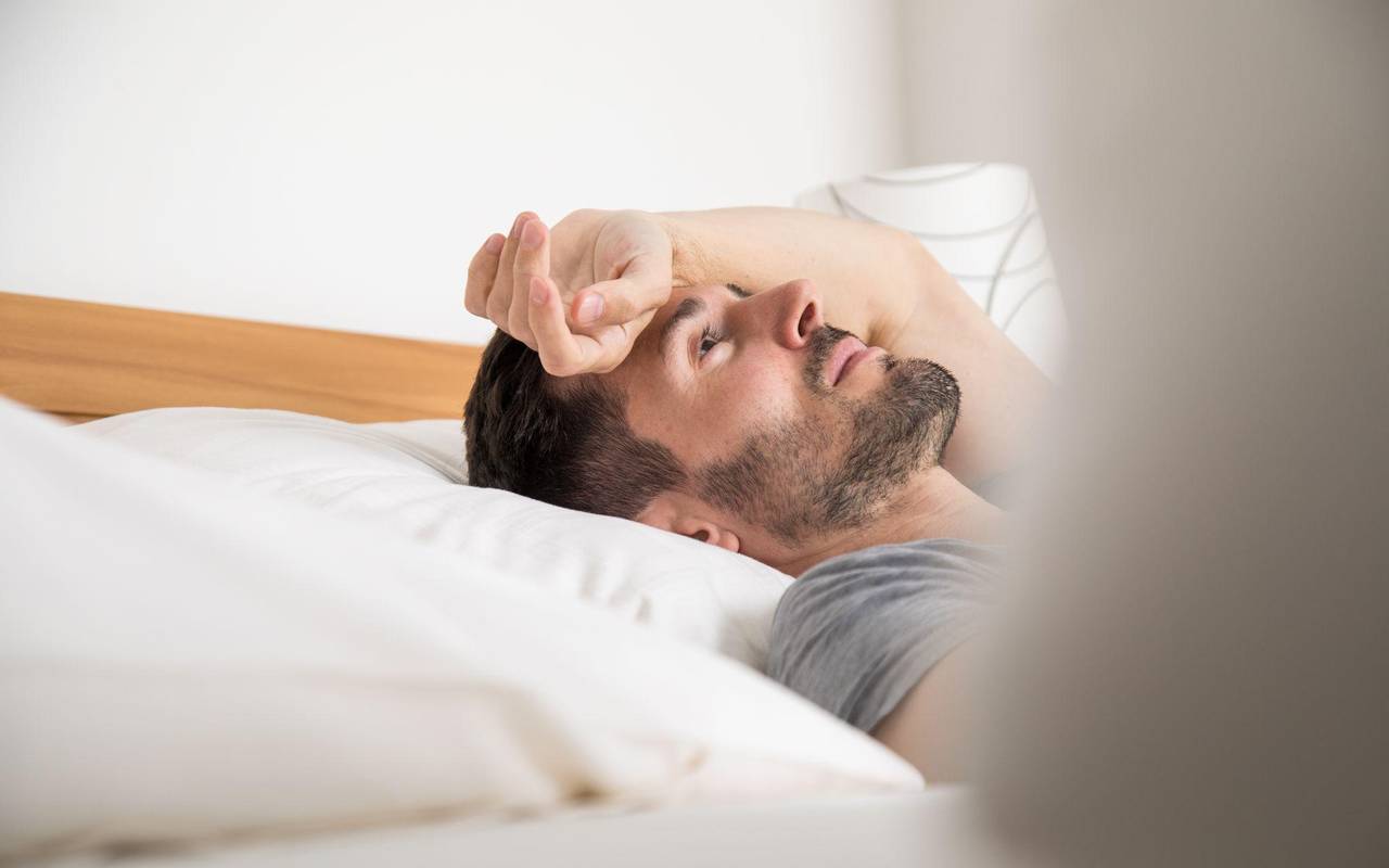 Mann liegt schlaflos im Bett