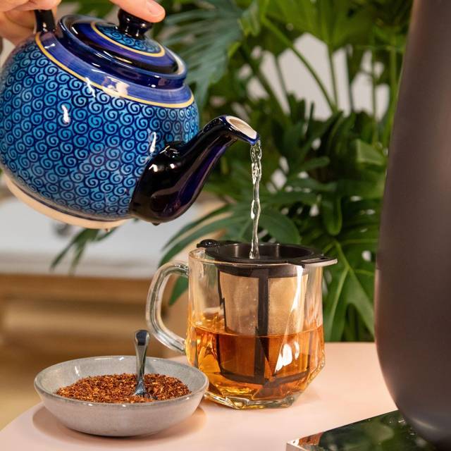 Ein Mann macht sich ein Glas Rooibos-Tee mit heißem Wasser