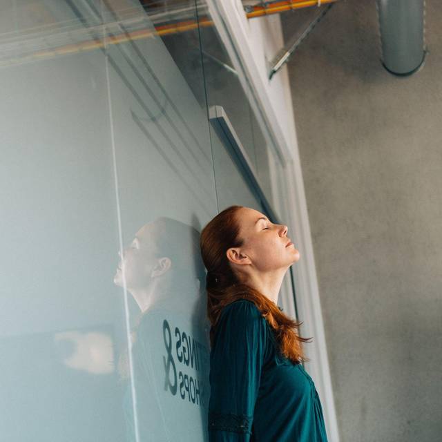Eine Frau lehnt erschöpft an einer Glaswand im Büro