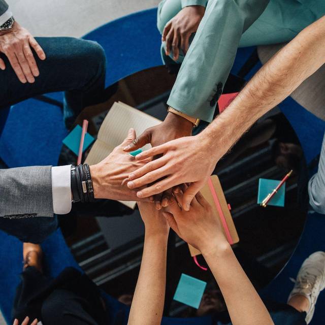 Gruppe Kolleginnen und Kollegen legen die Hände aufeinander
