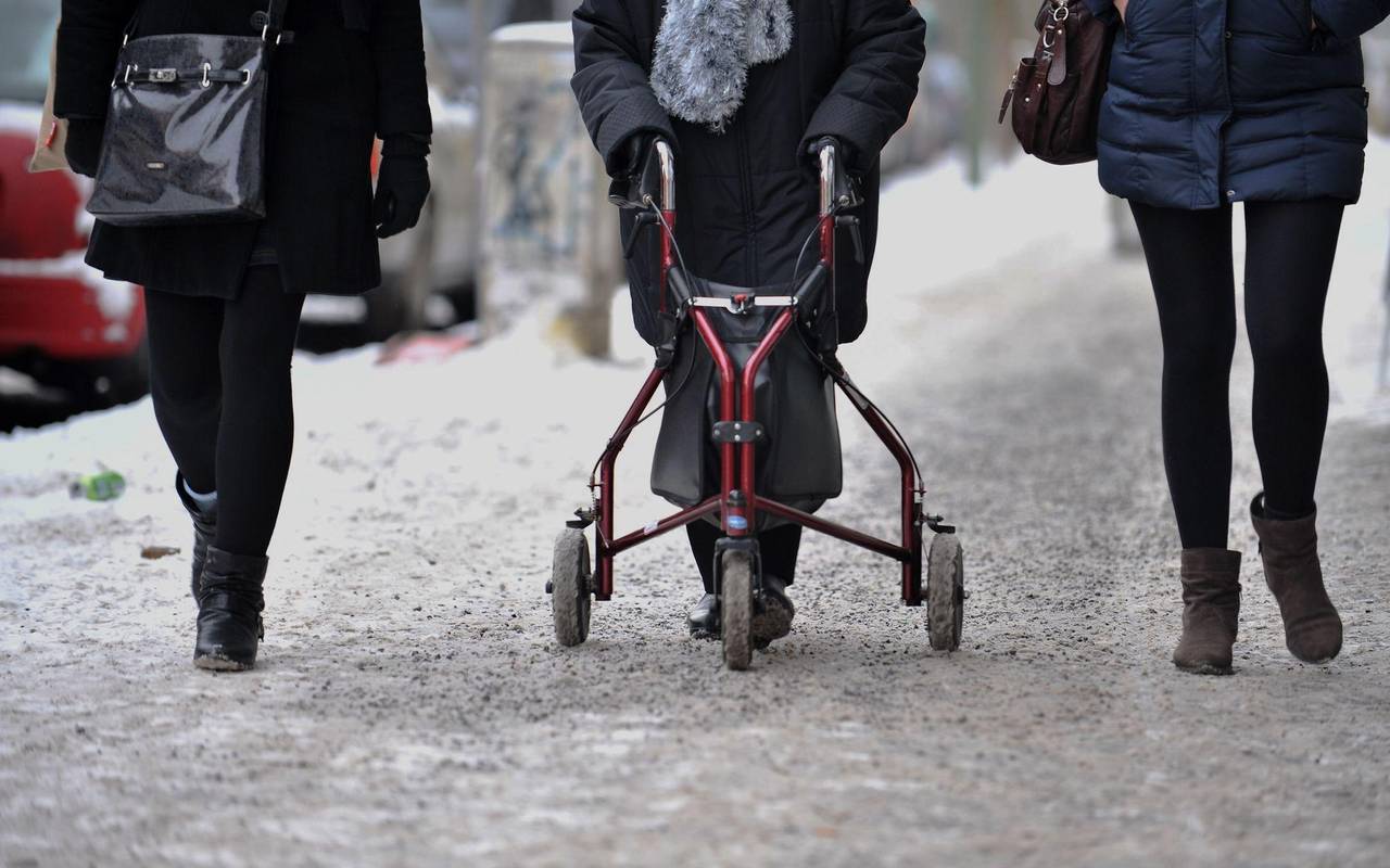 Ein Frau geht mit Rollator auf einem schneebedeckten Gehweg