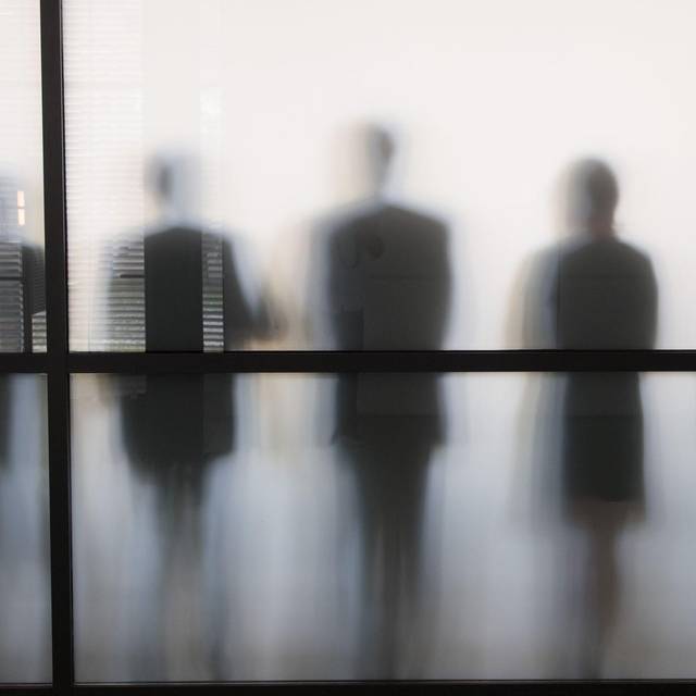 Personen stehen hinter eine Glasscheibe in einem Büro