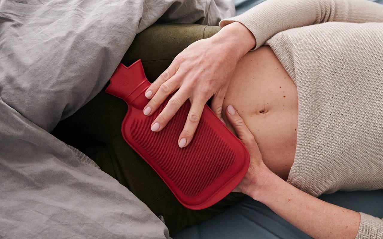Eine Frau hält sich eine Wärmflasche an den Unterbauch