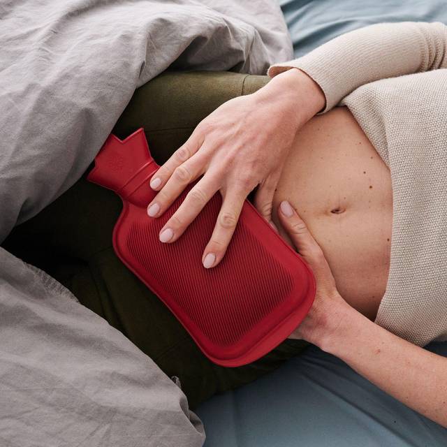 Eine Frau hält sich eine Wärmflasche an den Unterbauch