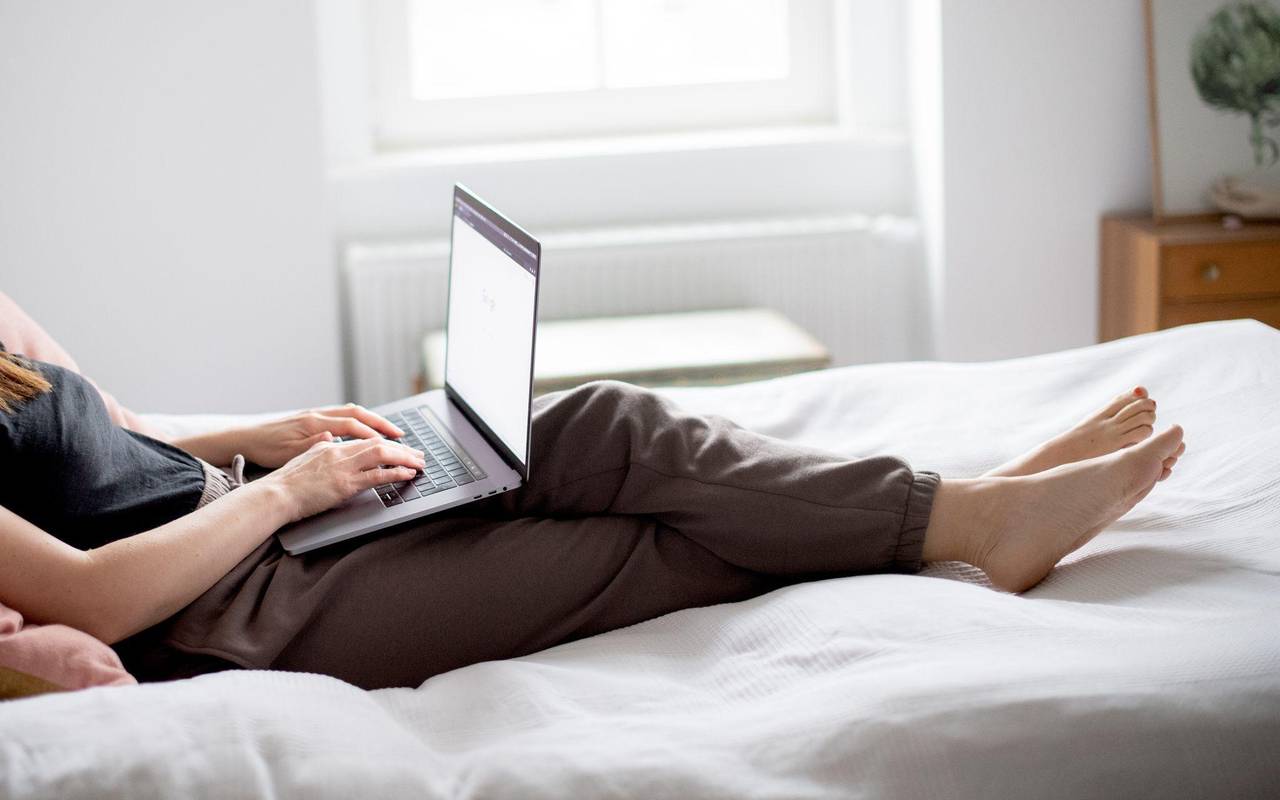 Eine Frau sitzt auf einem Bett und arbeitet mit ihrem Laptop