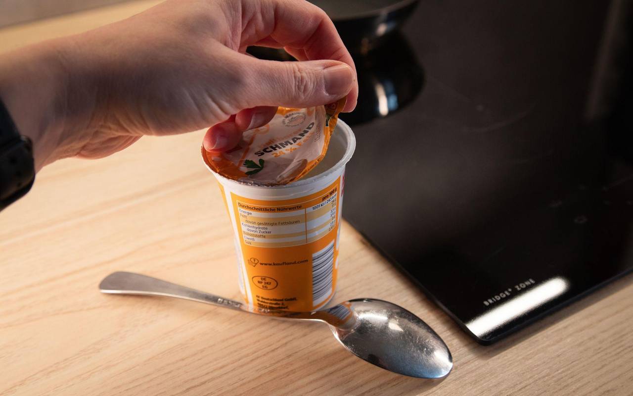 Frau öffnet einen Becher Schmand