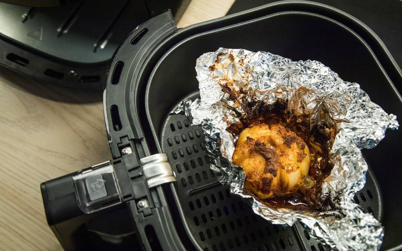 Eine in Alufolie gewickelte Zwiebel liegt in einem Airfryer