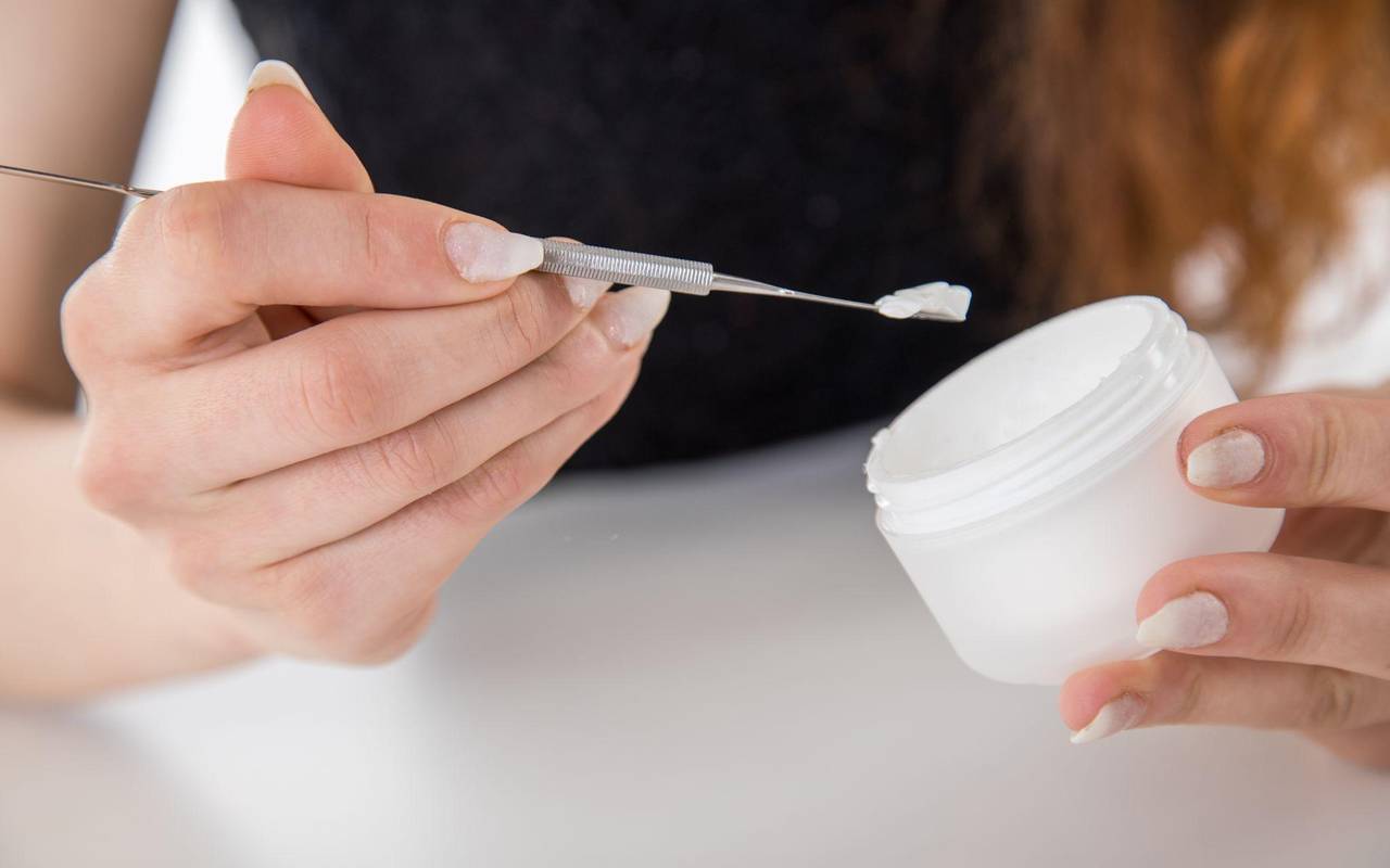 Eine Frau entnimmt mit einem Spatel Creme aus einem Tiegel