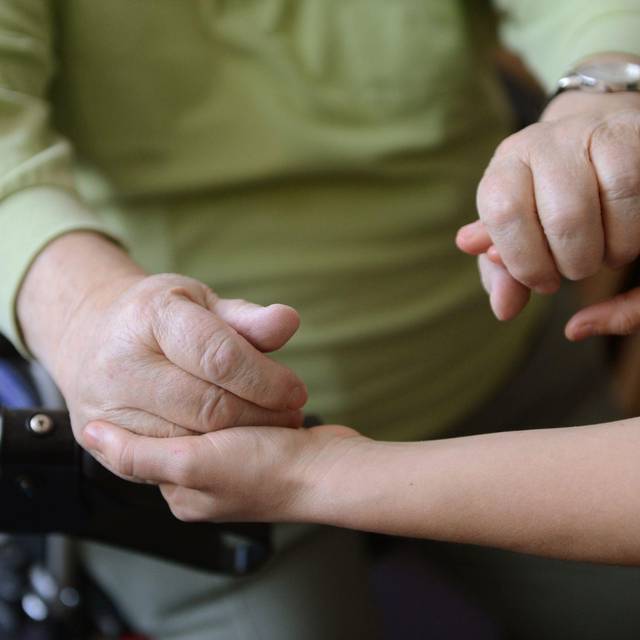 Eine junge Frau hält die Hände eines alten Mannes
