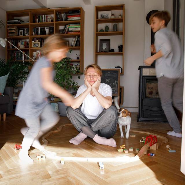 Gestresste Mutter sitzt zwischen dem Spielzeug ihrer Kinder