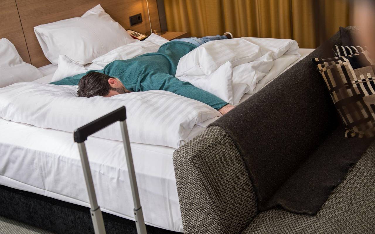 Ein Mann liegt erschöpft auf einem Bett in einem Hotelzimmer