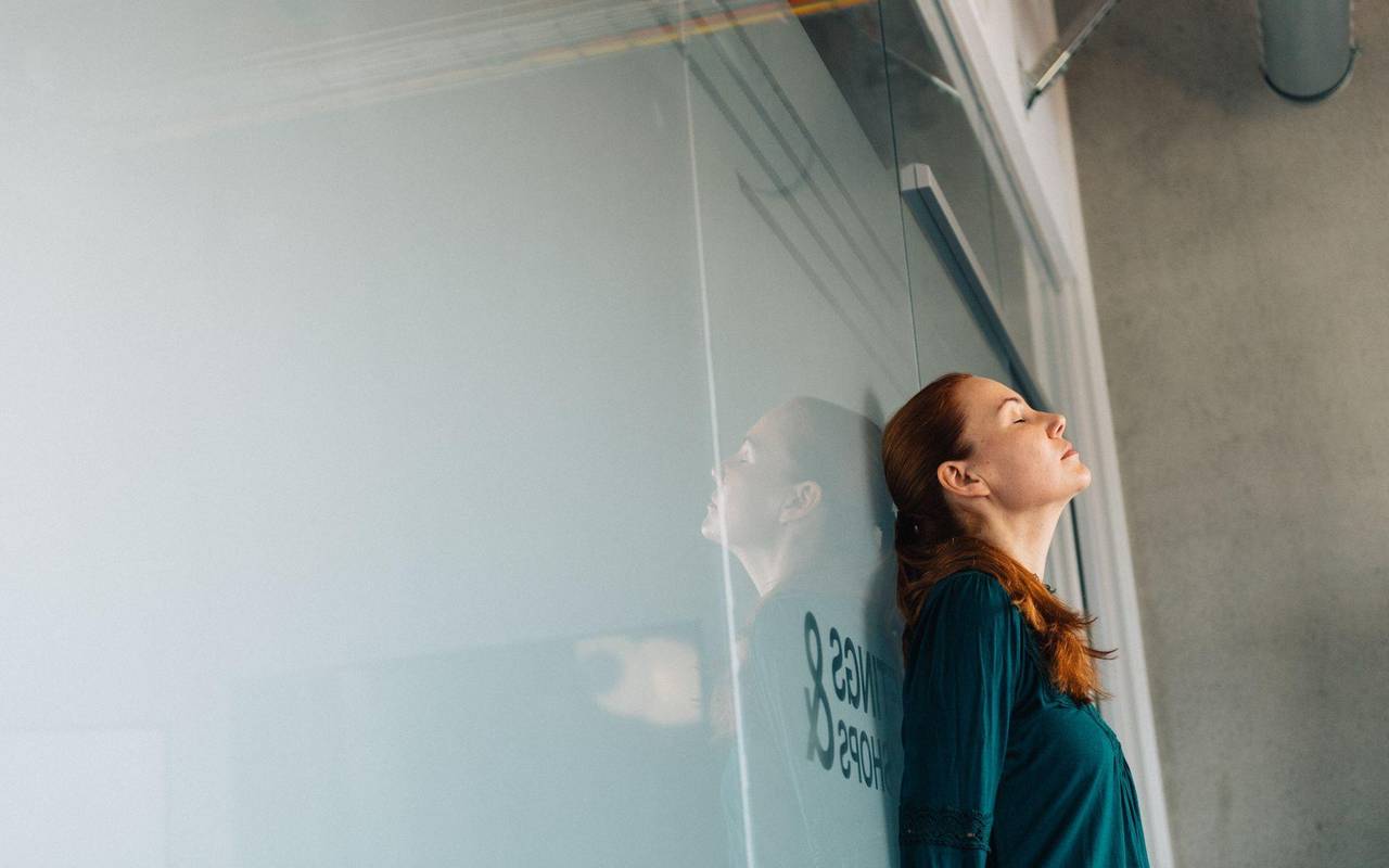 Eine junge Frau lehnt nachdenklich an einer Glaswand