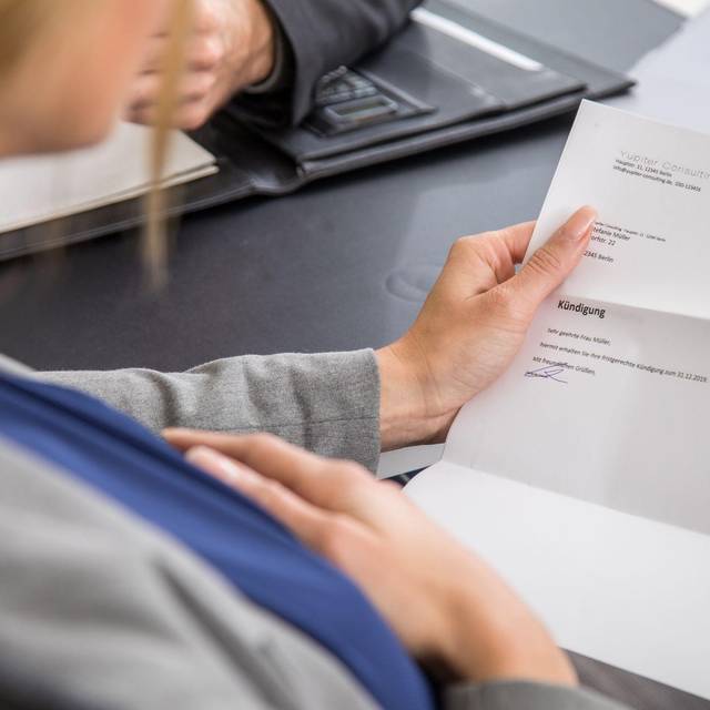 Eine schwangere Frau hält eine Kündigung in der Hand