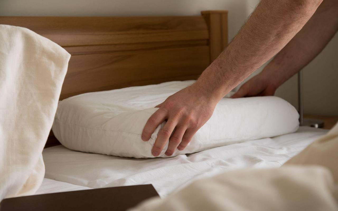 Eine Person greift nach einem flachen Kopfkissen