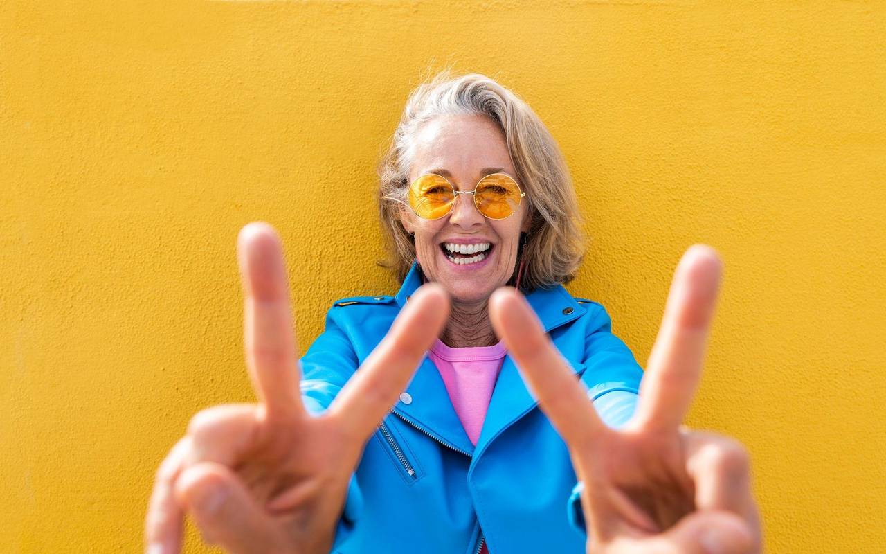 Frau lächelt in die Kamera und zeigt Peace-Zeichen