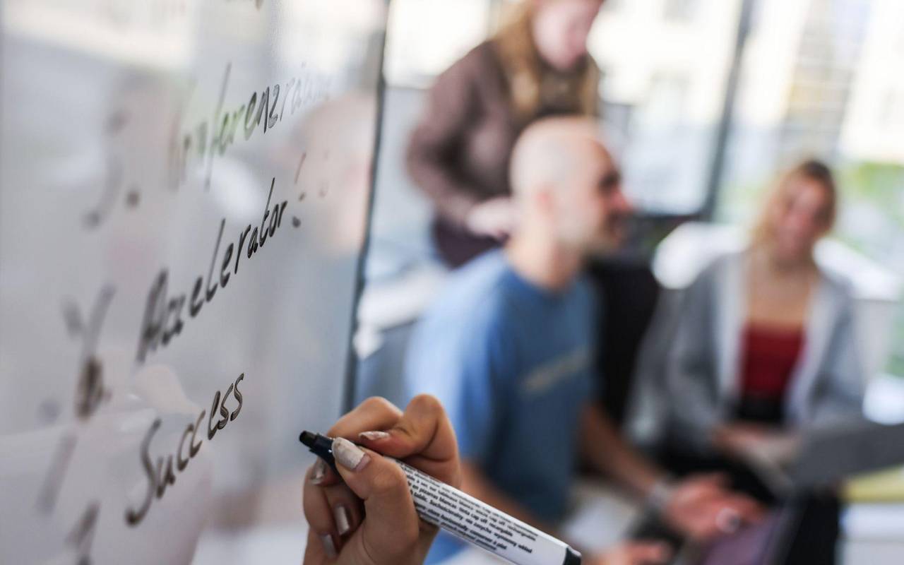 Eine Person schreibt mit schwarzem Marker auf ein Whiteboard