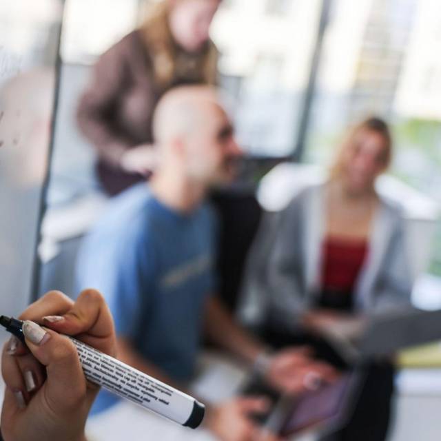 Eine Person schreibt mit schwarzem Marker auf ein Whiteboard