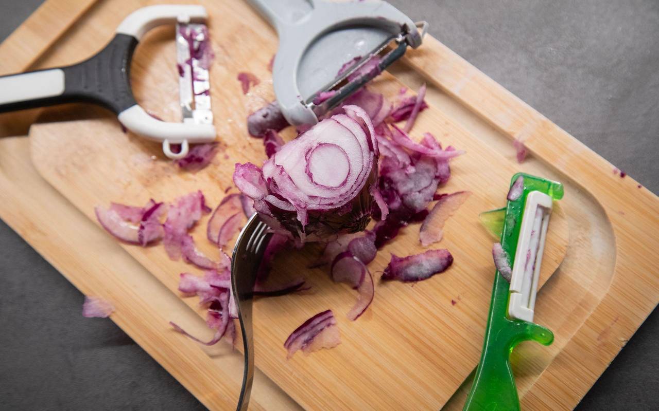 Verschiedene Sparschäler liegen neben einer Zwiebel