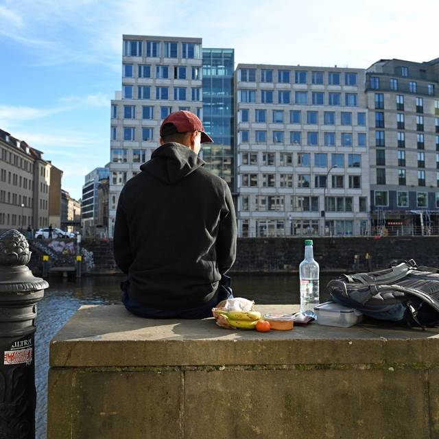 Ein Mann sitzt in der Sonne auf einer Mauer an der Spree