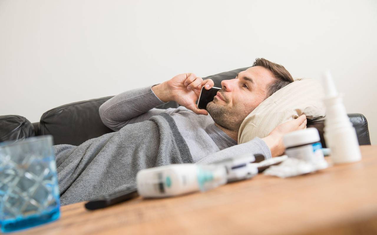 Ein Mann liegt krank auf einem Sofa und telefoniert
