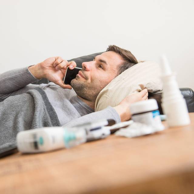Ein Mann liegt krank auf einem Sofa und telefoniert