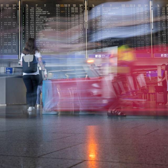 Passagiere gehen vor der Anzeigetafel im Flughafen entlang