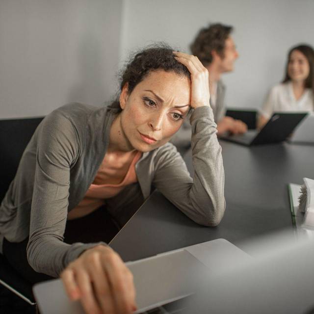 Frau sitzt grübelnd vor ihrem Laptop im Büro
