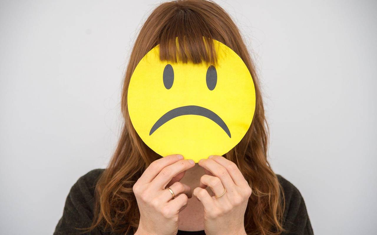 Eine Frau hält sich ein trauriges Smiley vor ihr Gesicht