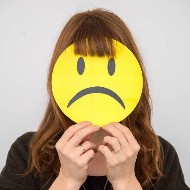 Eine Frau hält sich ein trauriges Smiley vor ihr Gesicht