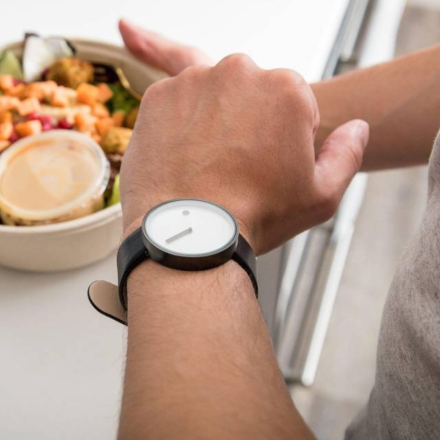 Mann mit einem Salat in der Hand schaut auf seine Armbanduhr