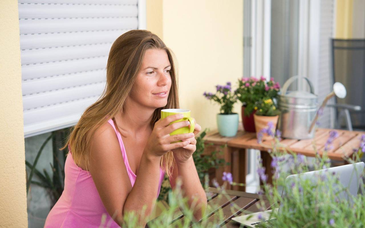 Frau sitzt auf einem Balkon und trinkt Kaffee