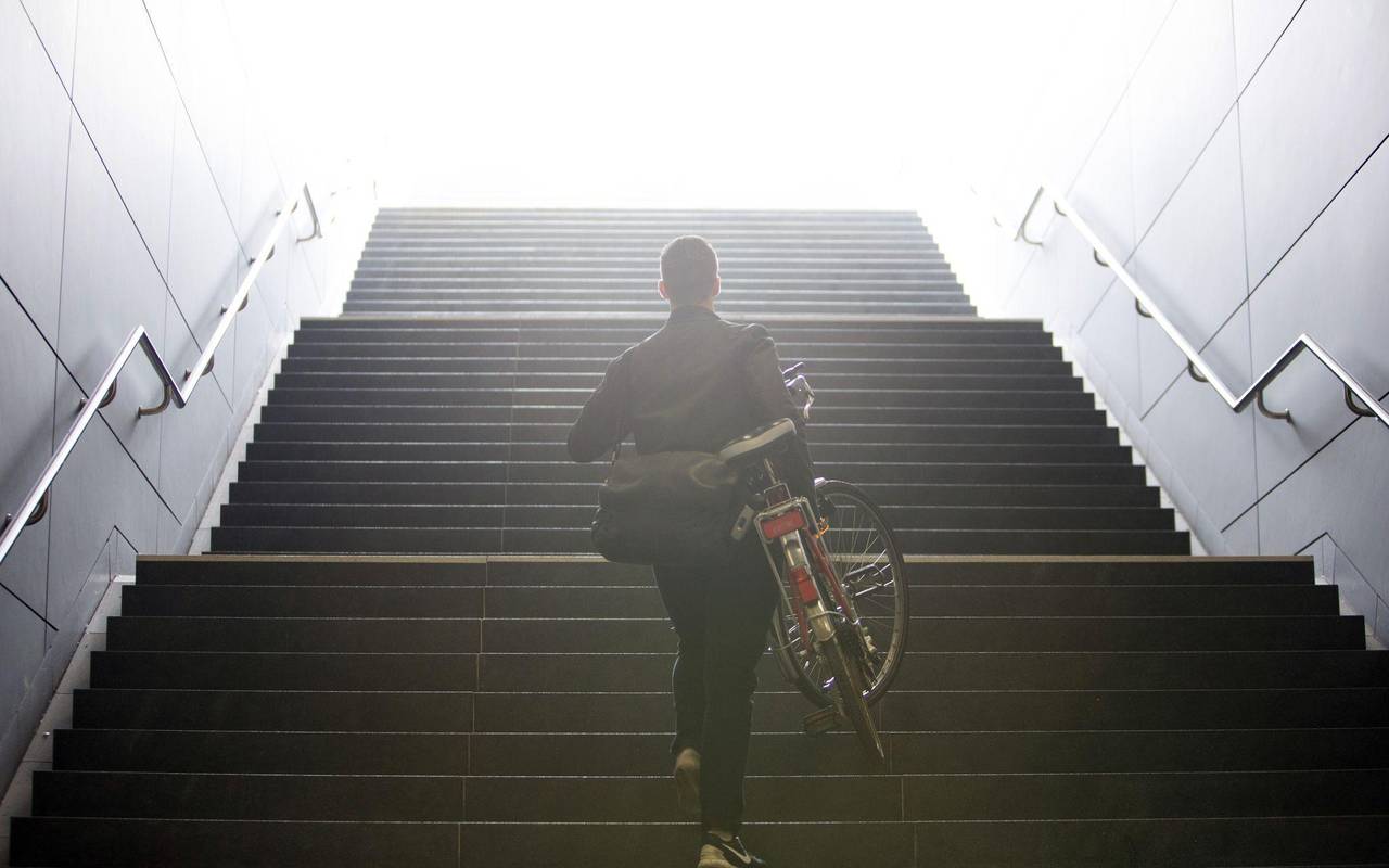 Mann trägt sein Fahrrad eine Treppe hinauf