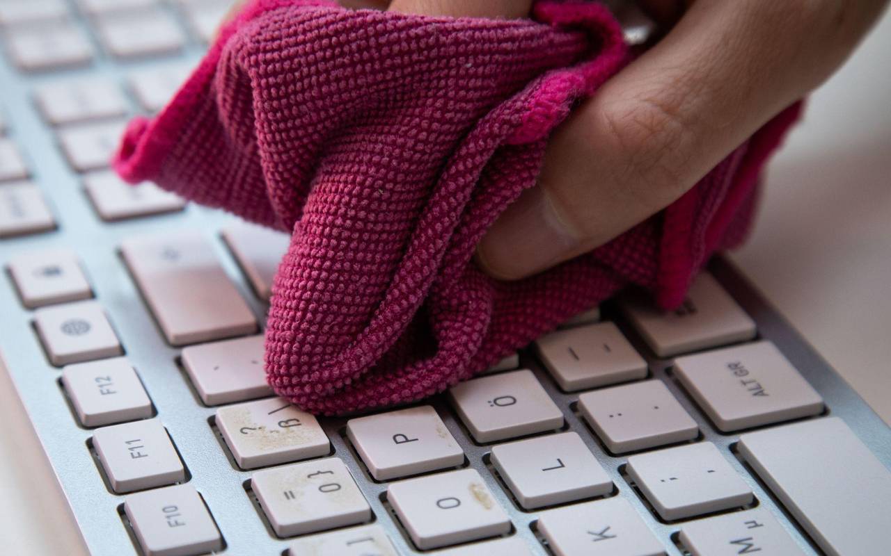 Ein Mann reinigt eine Tastatur mit einem Mikrofasertuch