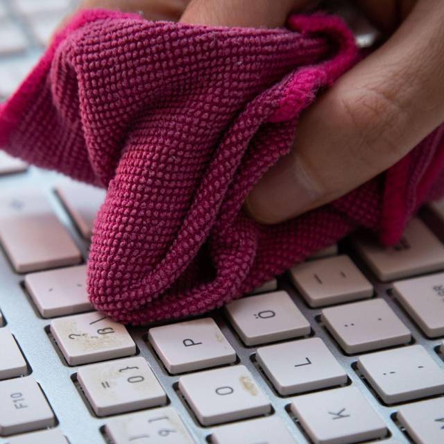 Ein Mann reinigt eine Tastatur mit einem Mikrofasertuch