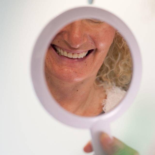 Frau schaut sich ihre Zähne in einem Handspiegel an
