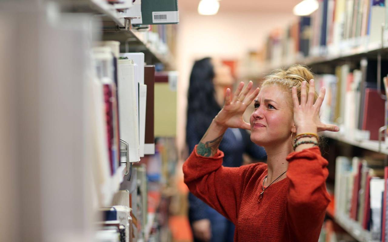 Frau steht wütend vor einem Bücherregal in der Unibibliothek
