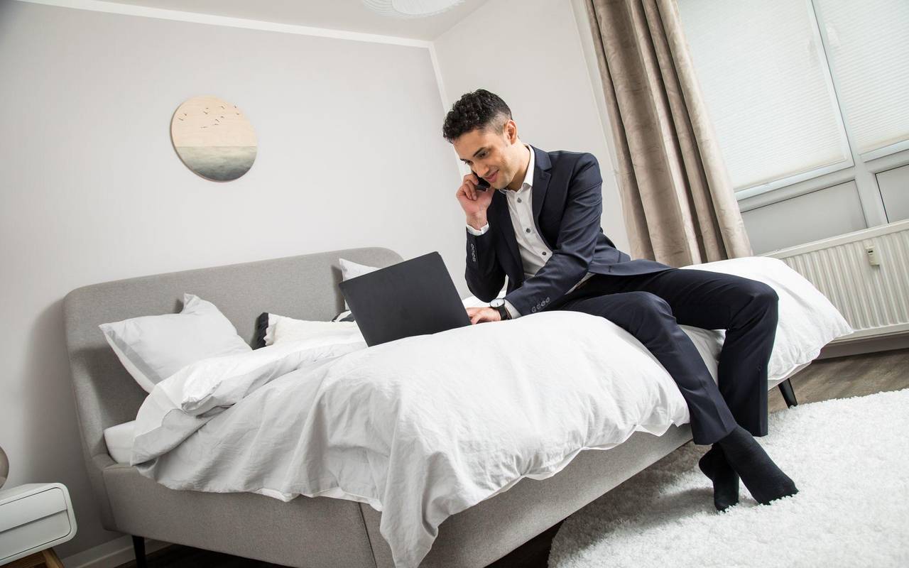 Ein Mann im Anzug sitzt auf einem Bett vor seinem Laptop