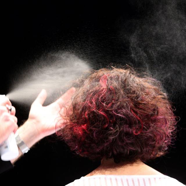 Ein Friseur sprüht einer Frau die Haare mit Haarspray ein