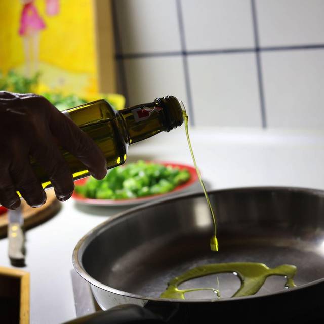 Frau gibt beim Kochen Olivenöl in eine Pfanne