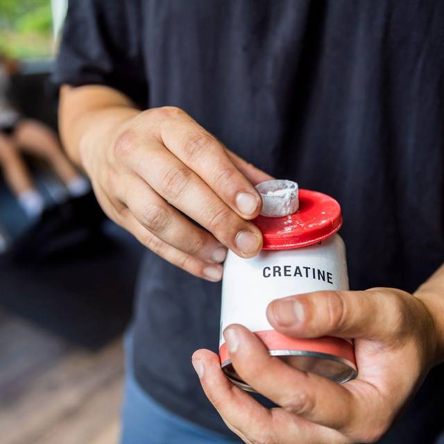 Ein Mann hält im Gym eine Packung Kreatin in seiner Hand
