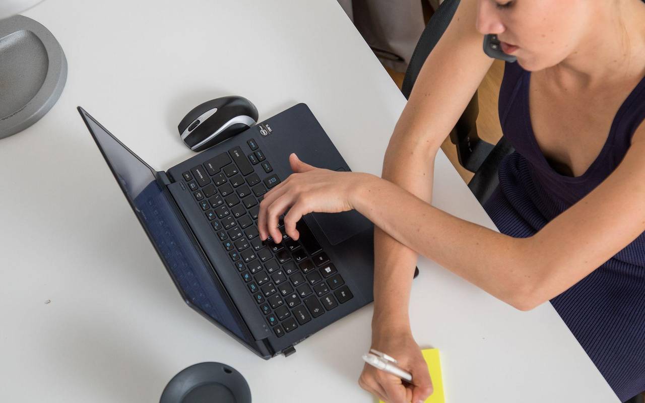 Eine Frau telefoniert, tippt auf Laptop und schreibt Notiz