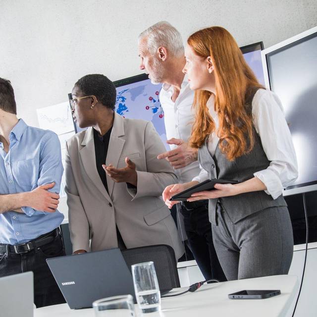 Eine Kollegin hebt die Uhr in einem Meeting mit anderen Kollegen