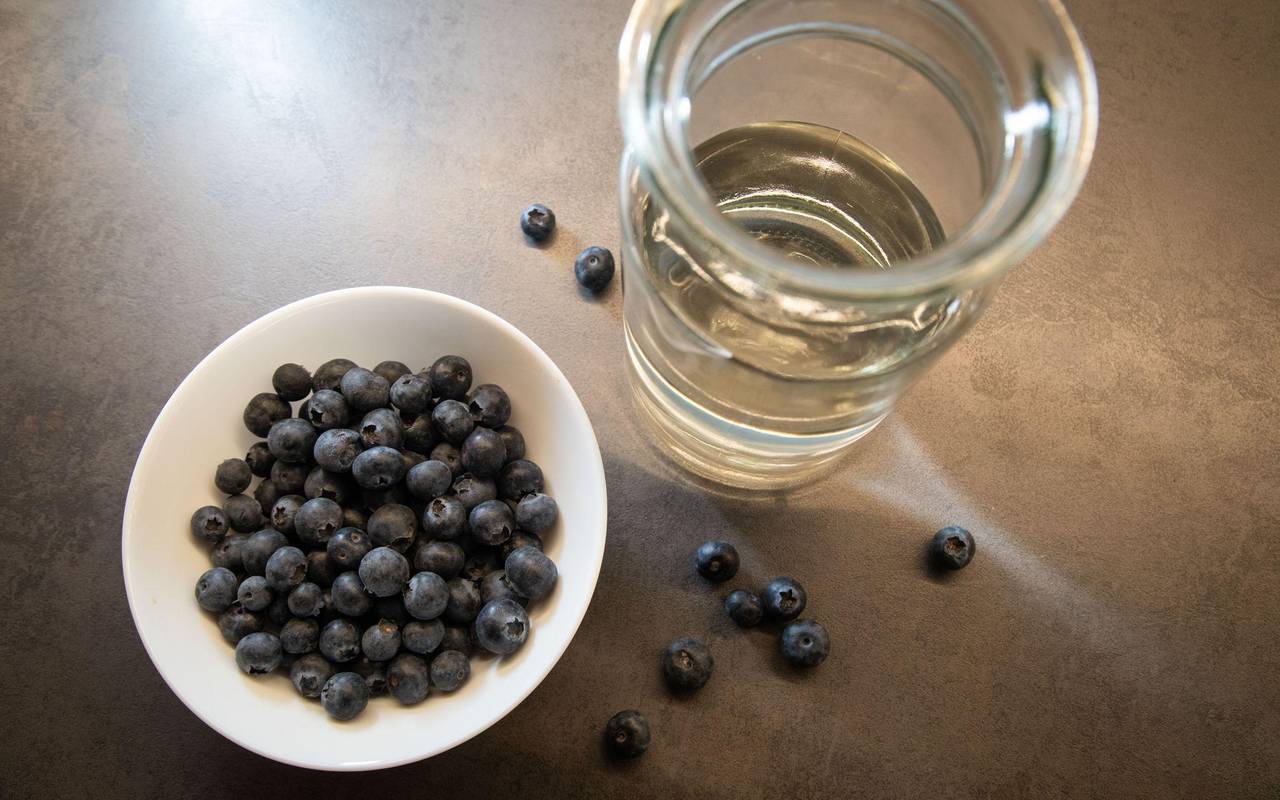 Blaubeeren liegen in einer Schale neben einem Glas Wasser